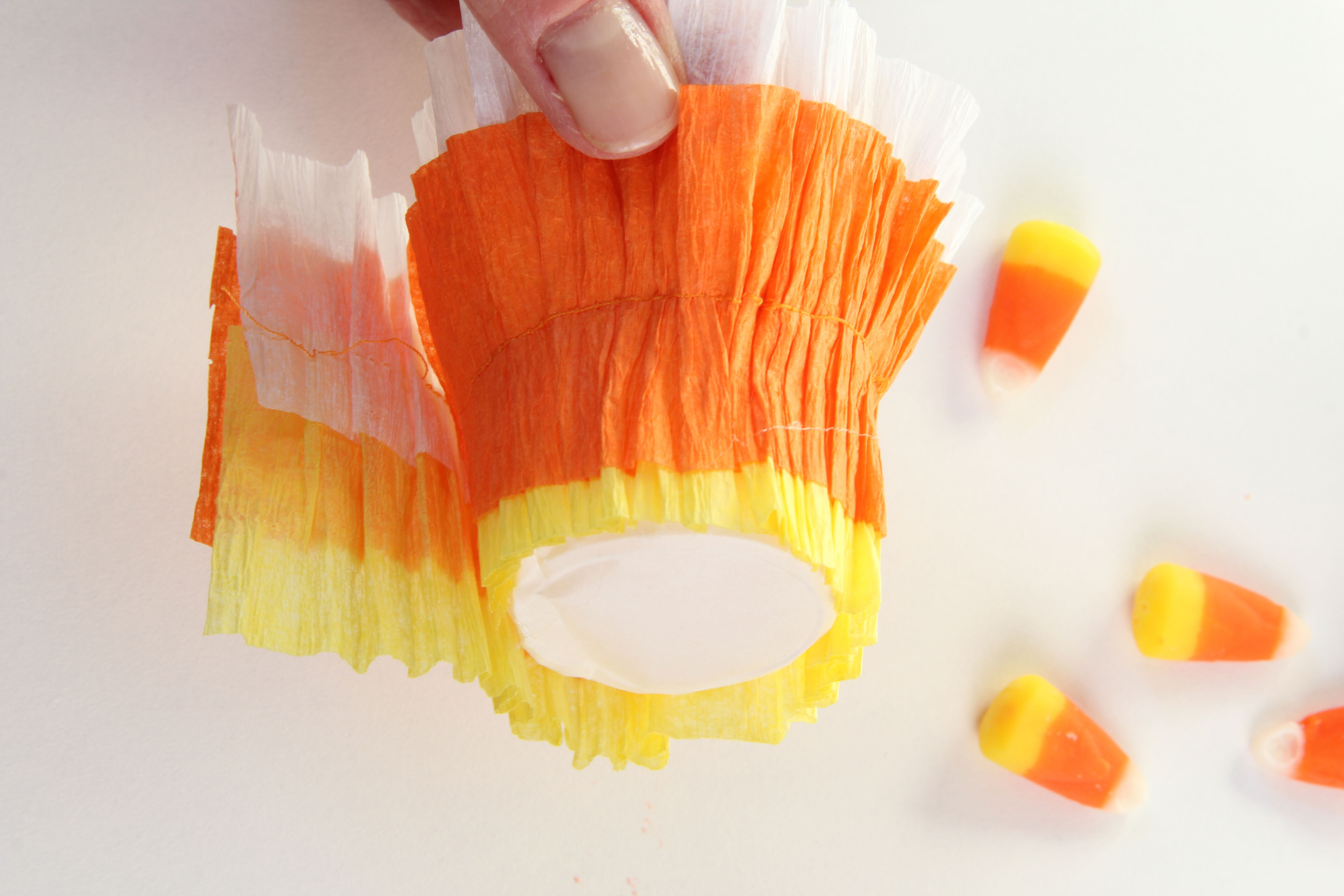 Assemble the DIY candy Corn Baskets with a hot glue gun. Wrap the sewed crepe paper to the cup and glue down. Super easy and Fun to make!