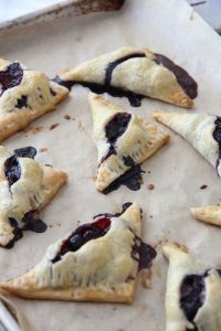 Blueberry blackberry turnovers fresh out of the oven on a parchment lined baking sheet. The fruit has released its juices on the pan.