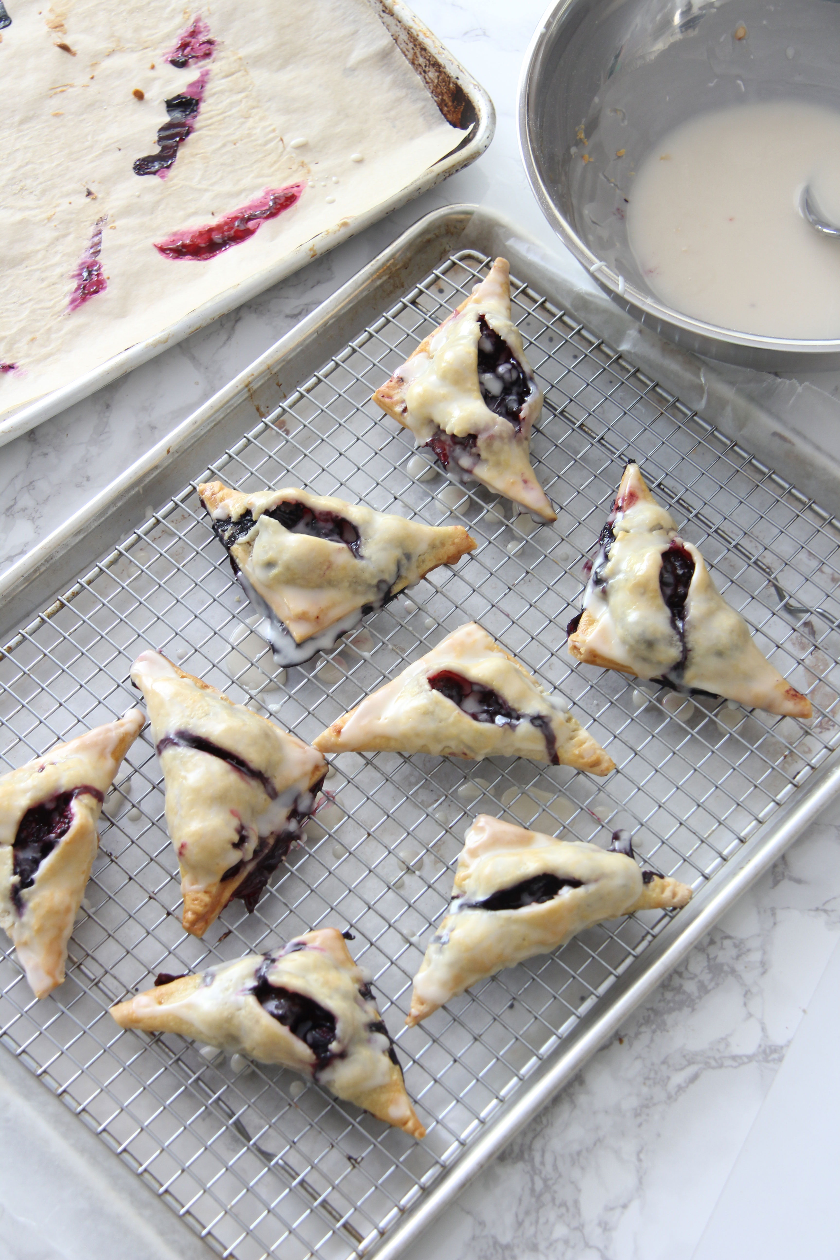 Glazing the blueberry blackberry turnovers by dipping them top down into a sugar mixture and placing them on a rack to cool  