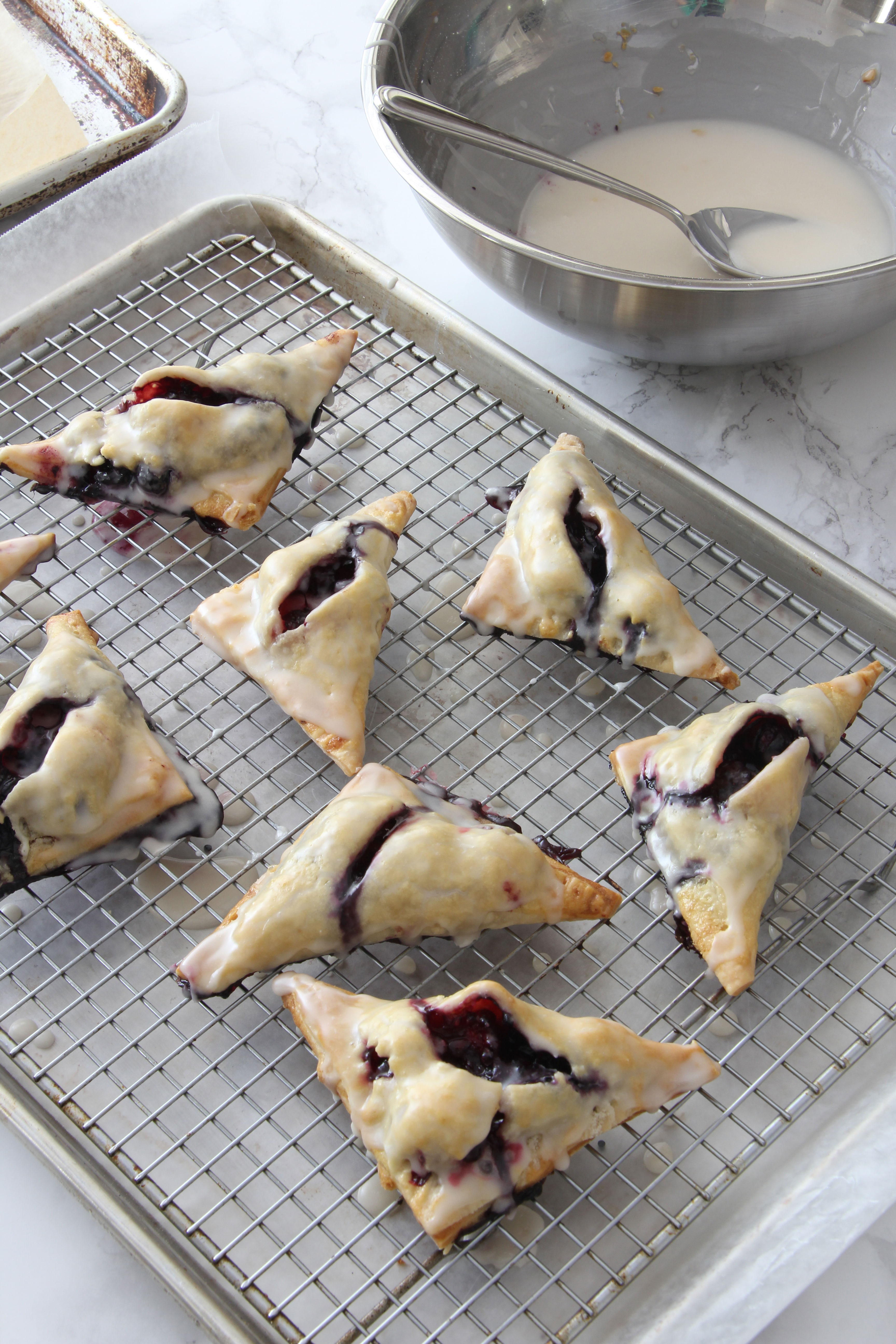 Glazing the blueberry blackberry turnovers by dipping them top down into a sugar mixture and placing them on a rack to cool  
