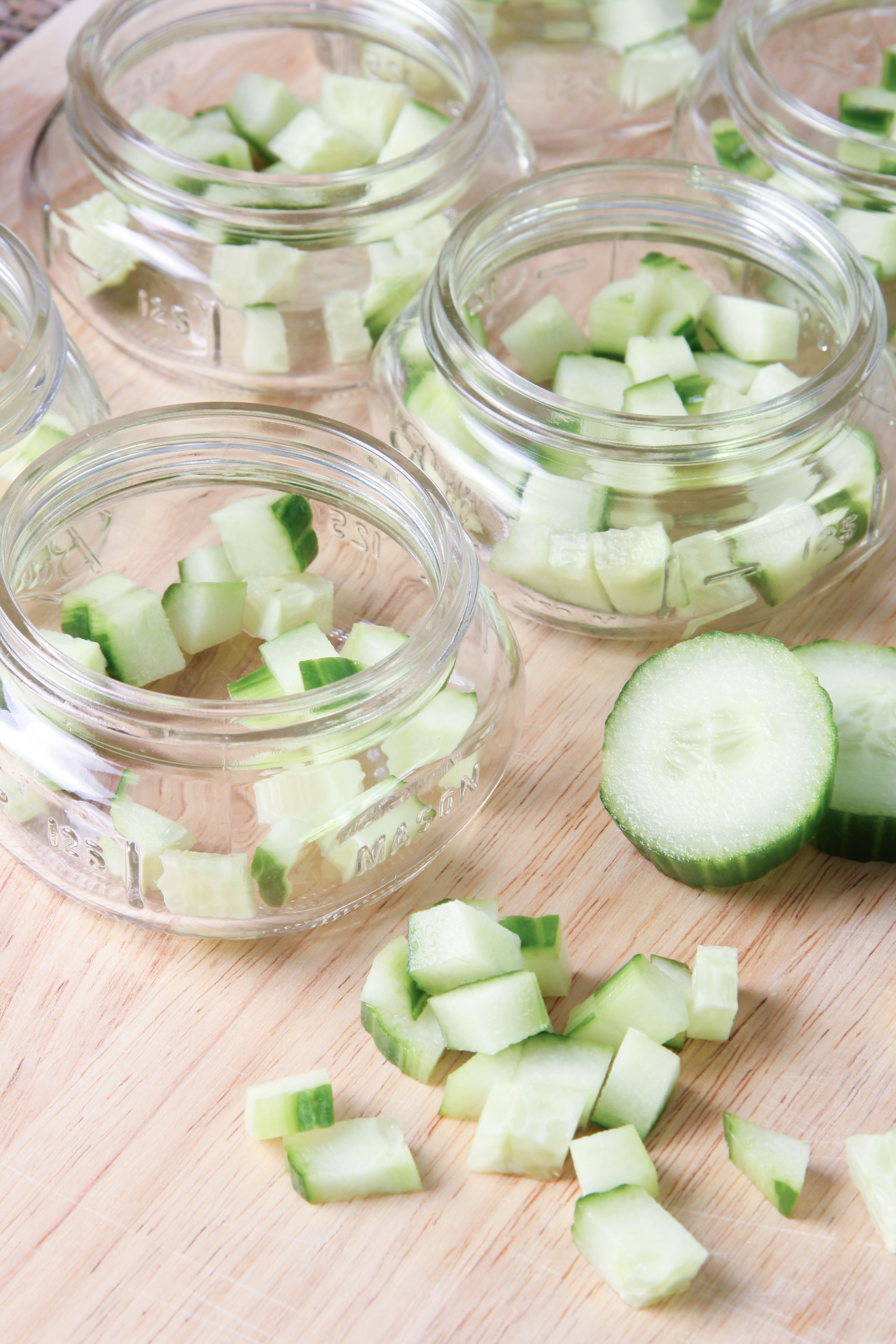 Diced Cucumbers placed in wide mouth mason jars for Chilled Cucumber Dill and Yogurt Soup. Preparing Individual portions of the soup for a beach picnic.