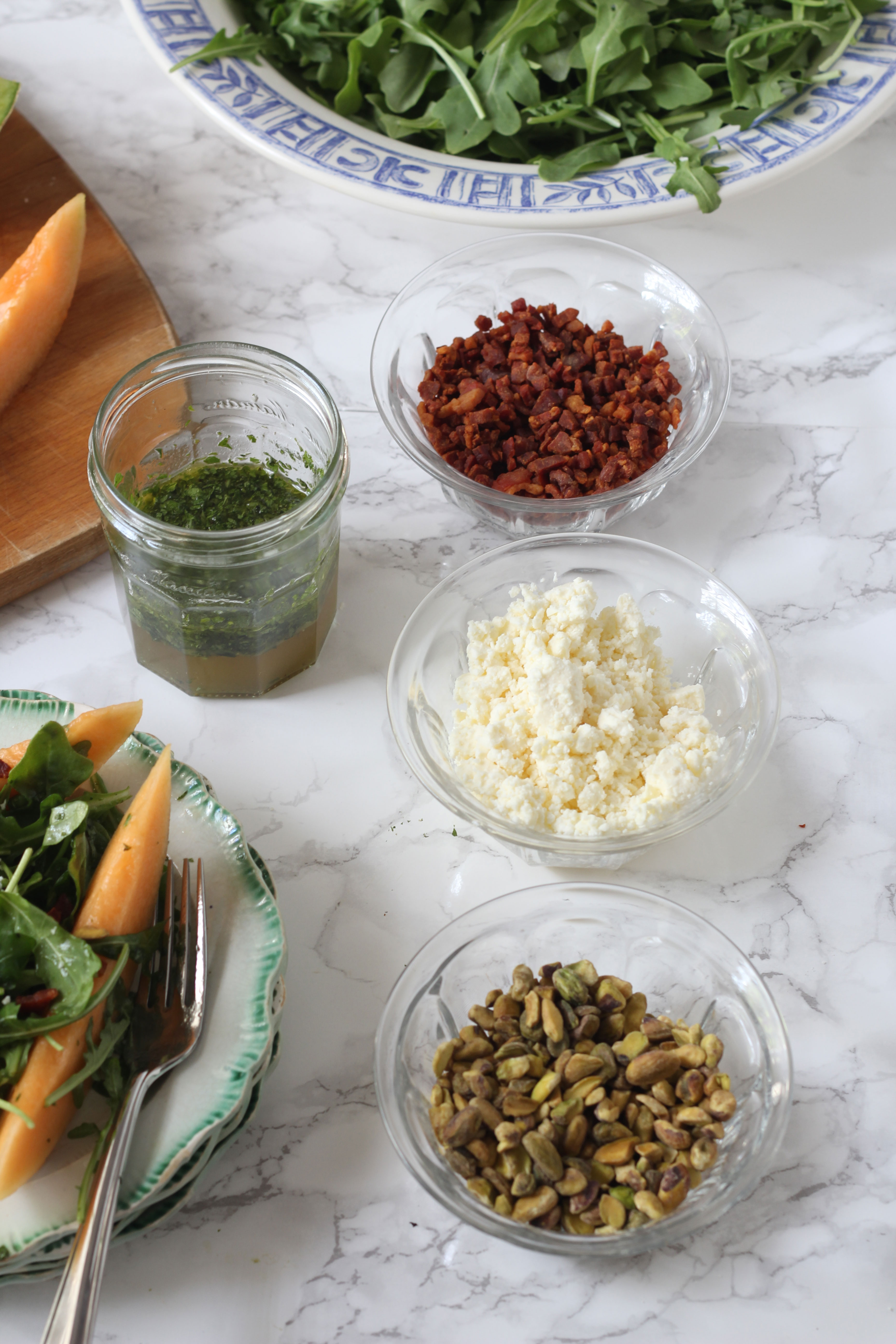 Everything you need to assemble a Melon and crispy prosciutto arugula salad. Including a fresh herb dressing, crumbled feta and chopped pistachios.